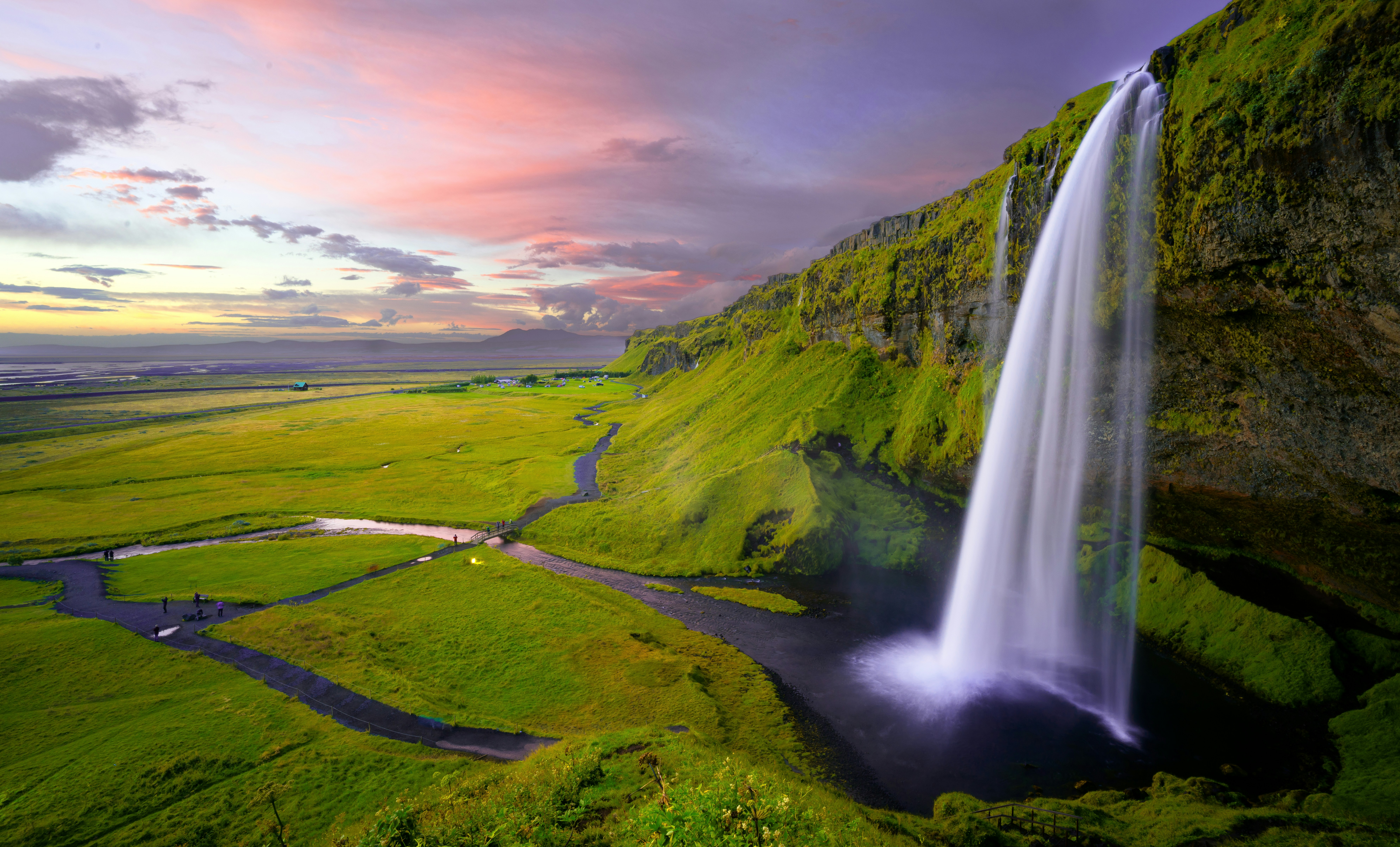 lush green fields surrounding a massive waterfall 